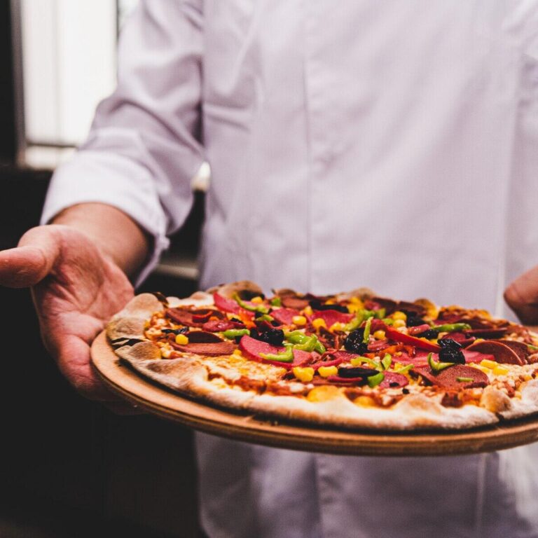 chef-holding-delicious-pizza-wooden-plate-kitchen_181624-44326